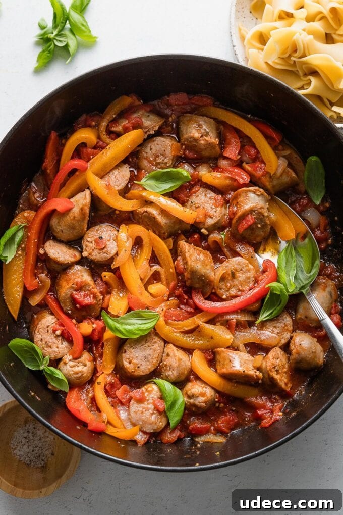 Italian Sausage with Peppers & Onions in Savory Tomato Sauce 7 Overhead image of saucy Italian sausage and peppers with tomatoes and garlic in a deep-sided all-black cast iron skillet.
