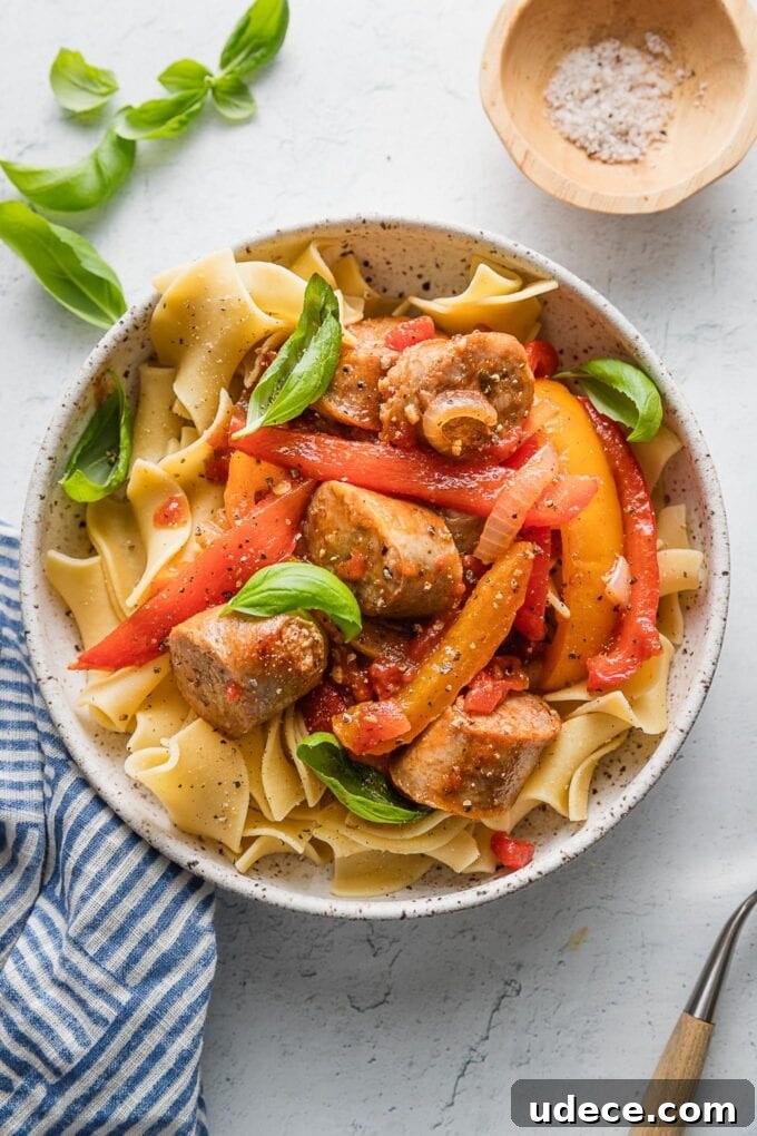 Italian Sausage with Peppers & Onions in Savory Tomato Sauce 8 Countertop set with a bowl of Italian sausage, peppers, and onions in a light tomato garlic sauce, with fresh basil and extra sea salt nearby for sprinkling and seasoning to taste.