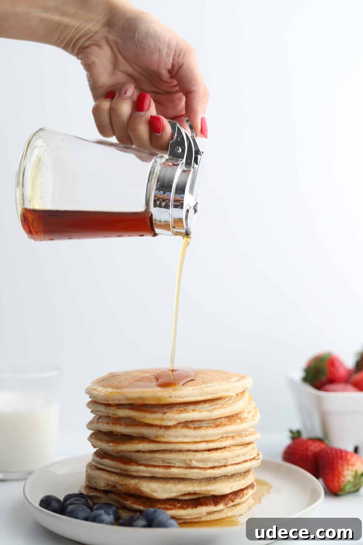 High-Protein Cottage Cheese Pancakes Recipe 2 a hand pouring syrup over a stack of pancakes with blueberries on the side.