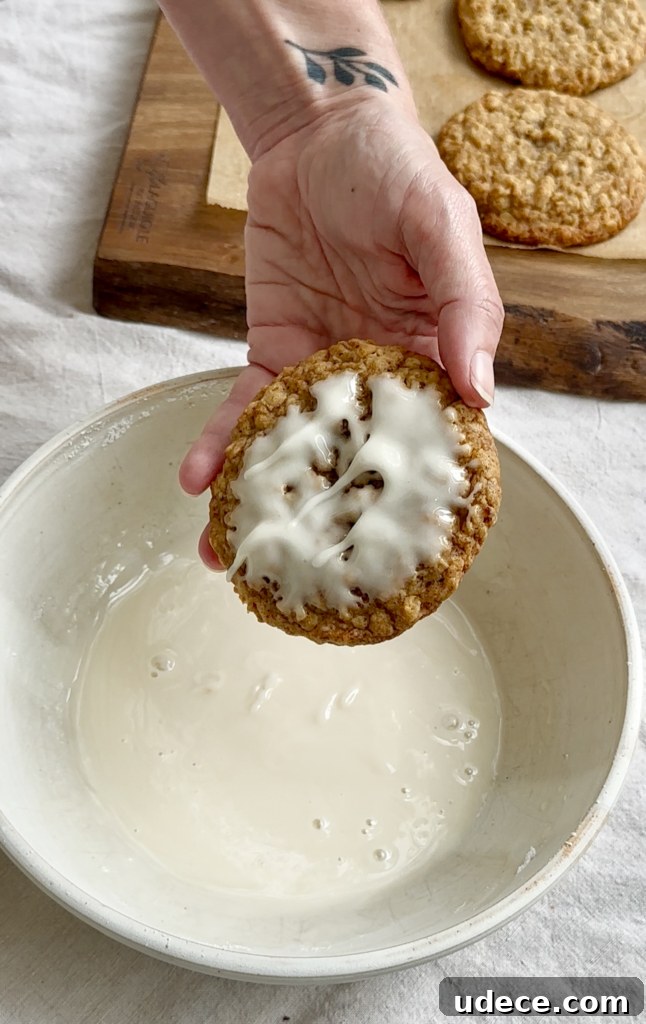 Hand holding an iced cookie over a bowl of vanilla icing.