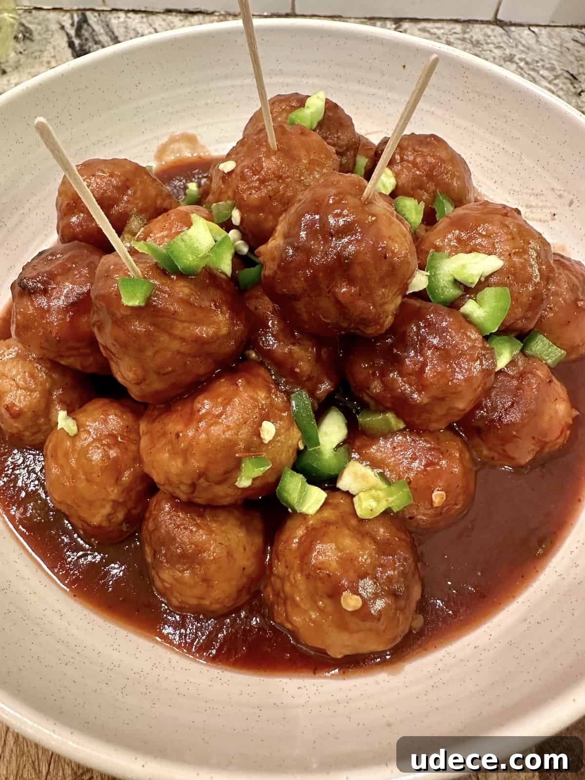 Sweet and Spicy Cranberry Jalapeño Meatballs Recipe 8 Cranberry meatballs in a serving bowl with diced peppers.