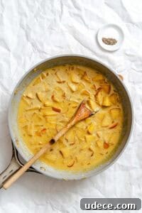 Creamy Apple Curry Recipe with Warm Spices and Coconut Milk 15 Process shot showing stirring ingredients in pan.