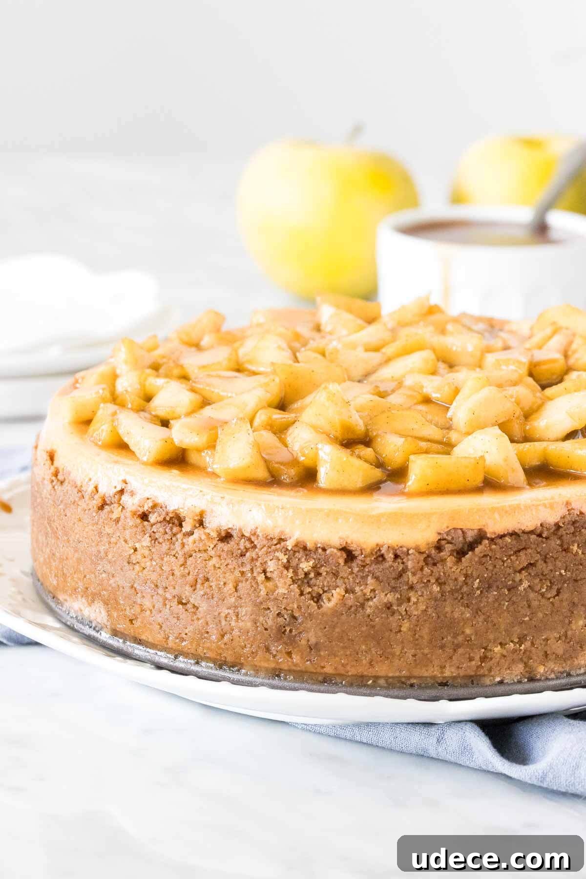 Caramel Apple Cheesecake Recipe with Crunchy Streusel Topping 3 Round cheesecake topped with chopped cinnamon apples on a plate.