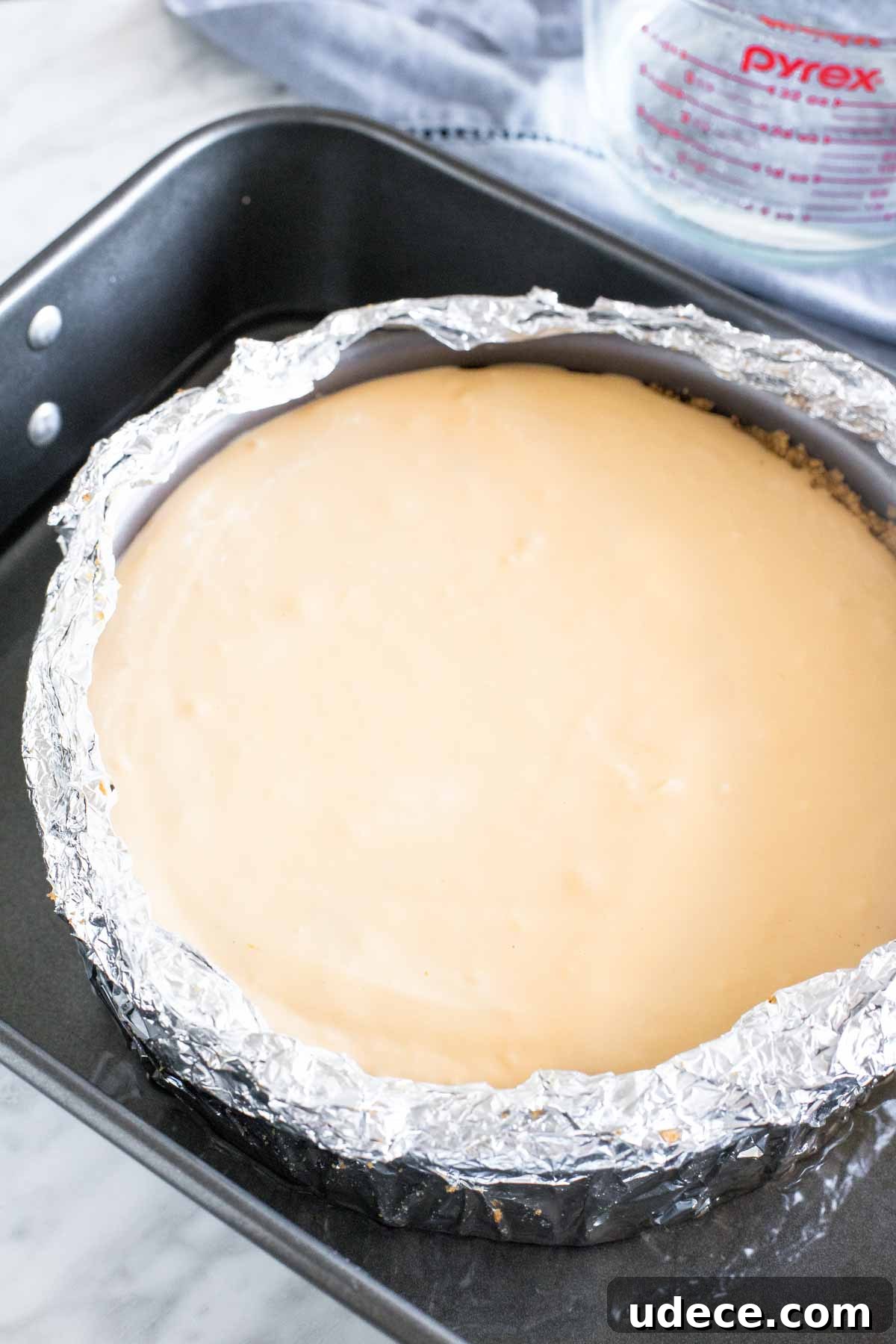 Caramel Apple Cheesecake Recipe with Crunchy Streusel Topping 4 Unbaked cheesecake in a springform pan wrapped in tinfoil in a large roasting pan.