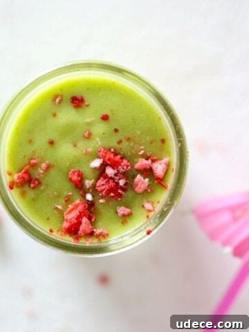 Top view of a green smoothie in a glass mason jar topped with crushed dried strawberry pieces.