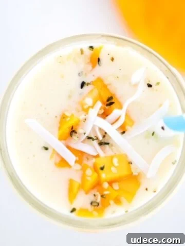 Creamy Mango Pineapple Smoothie topped with mango and coconut flakes with a blue and white striped straw.