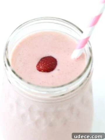 Strawberry banana smoothie in a glass jar, topped with a strawberry and served with a pink and white straw.