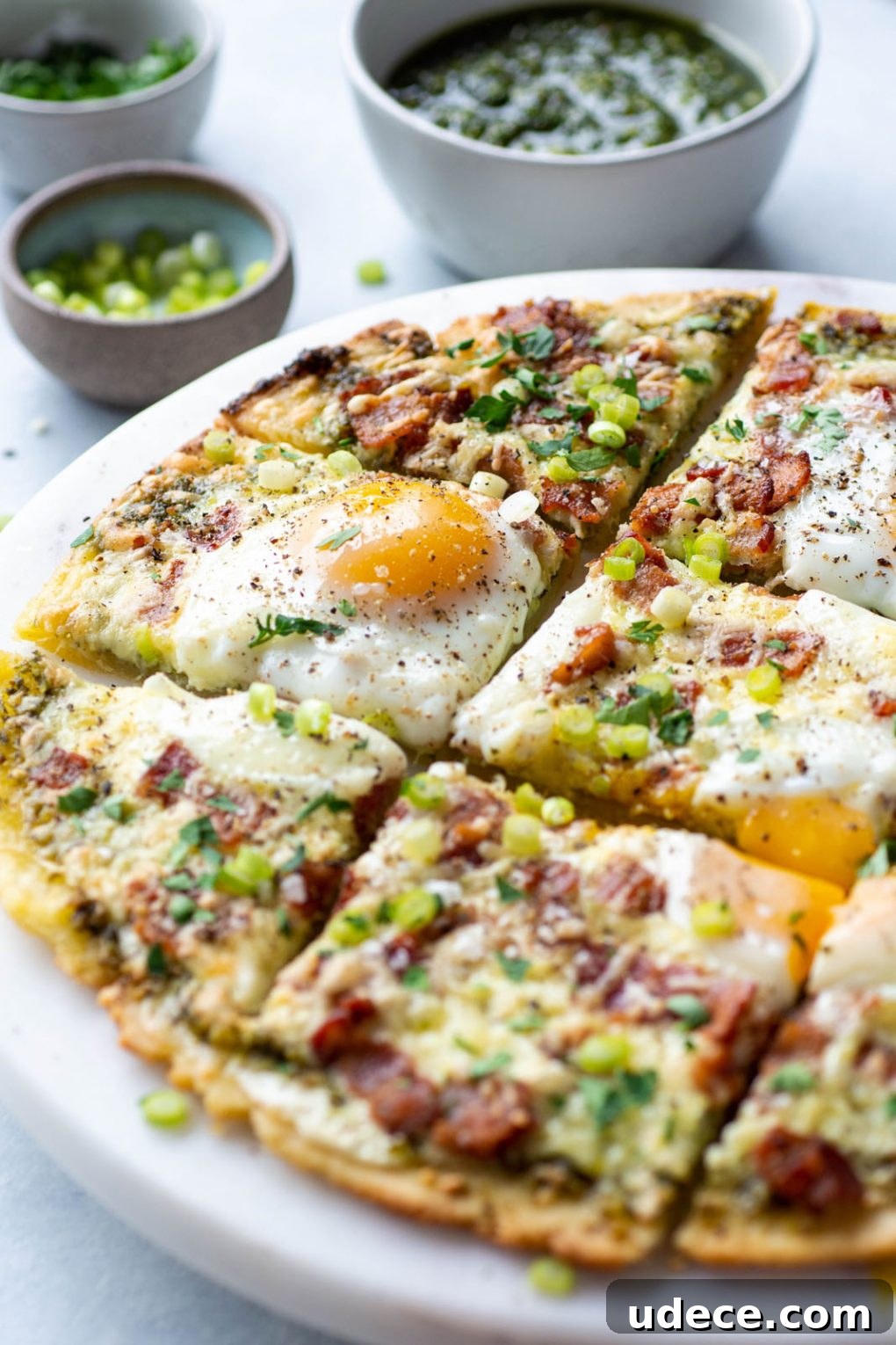 5-Ingredient Breakfast Pizza with Pesto and Crispy Bacon 2 Side angle view of a breakfast pizza with melted cheese, crispy bacon, sunny side up eggs, and fresh herbs and green onions.