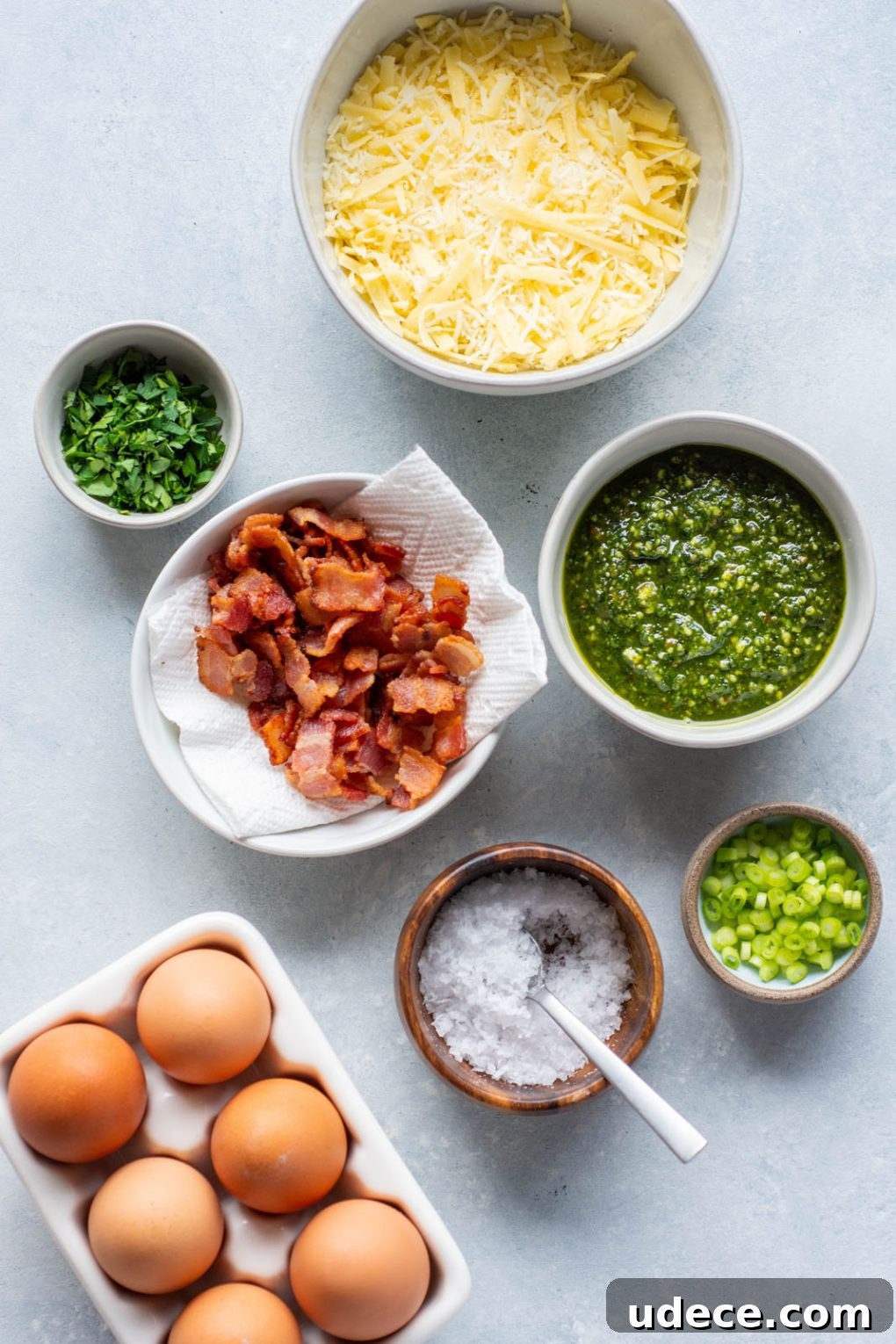 5-Ingredient Breakfast Pizza with Pesto and Crispy Bacon 5 Bowls holding cheese, pesto, herbs, green onions, cooked bacon, and eggs.