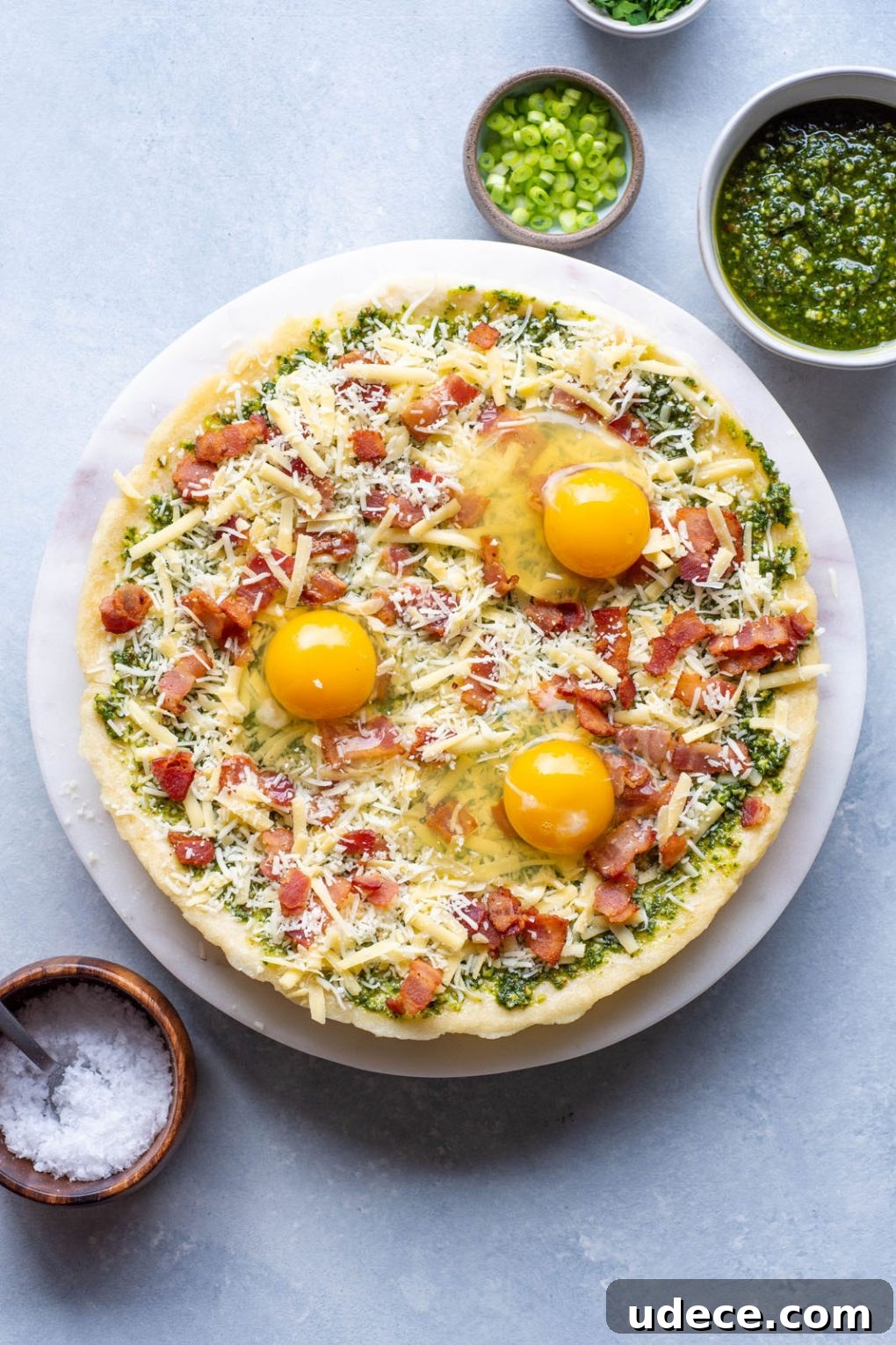 5-Ingredient Breakfast Pizza with Pesto and Crispy Bacon 6 Uncooked breakfast pizza topped with cheese, bacon, raw eggs, herbs and green onions.