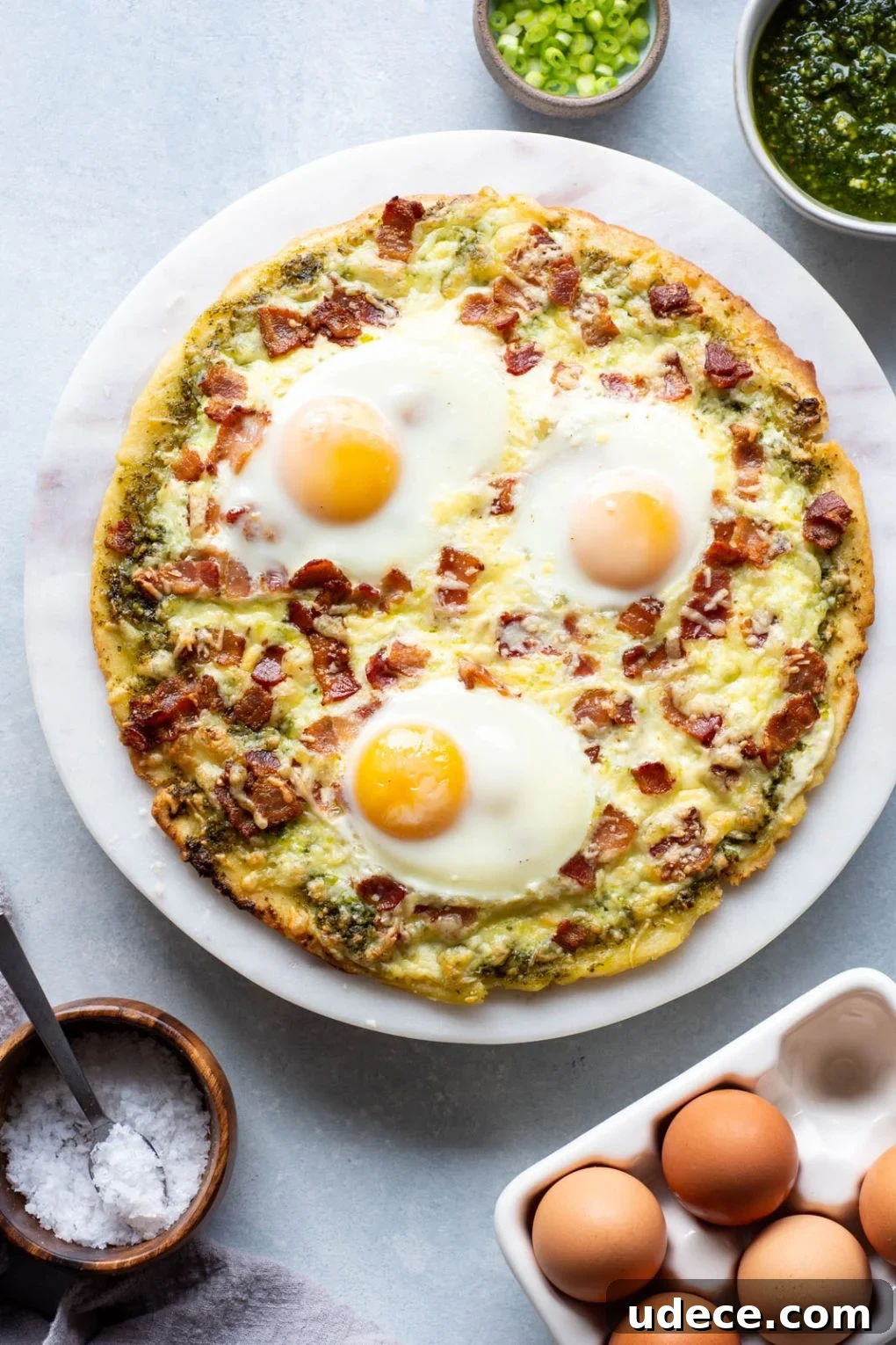 5-Ingredient Breakfast Pizza with Pesto and Crispy Bacon 7 Overhead shot of cooked breakfast pizza topped with cheese, bacon and sunny side up eggs.