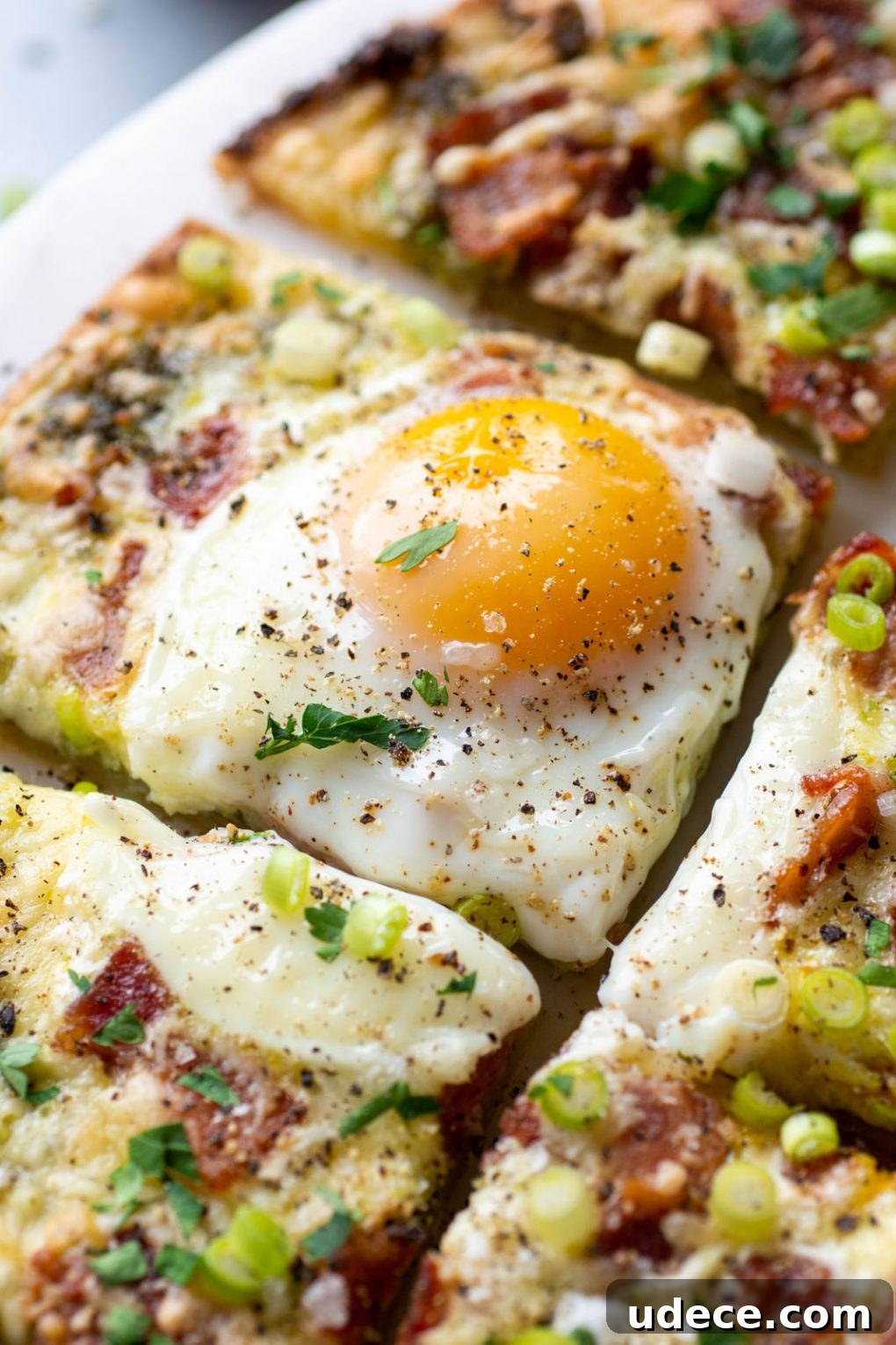 5-Ingredient Breakfast Pizza with Pesto and Crispy Bacon 8 Close up of a slice of breakfast pizza topped with melty cheese, bacon, a sunny side up egg, and fresh herbs.