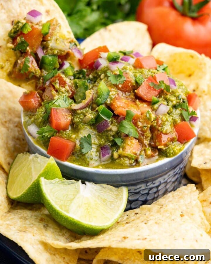 A chip dipping into a bowl of salsa pesto surrounded by tortilla chips.