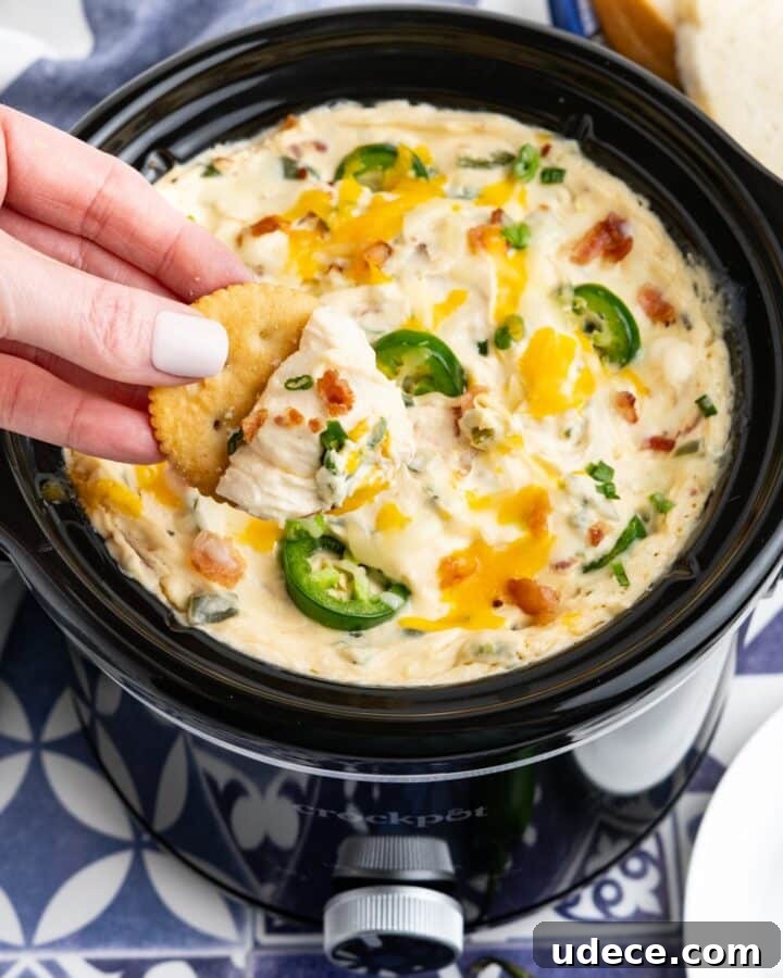 Crockpot jalapeno popper dip served up in a slow cooker with a hand dipping a cracker.