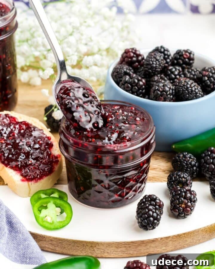 A jar of blackberry jalapeno jam with a spoonful of it held up over the jar.