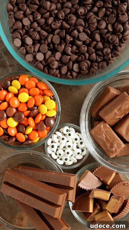 Halloween Candy Bark: Quick No-Bake Recipe for Kids' Treats 3 Overhead view of Halloween candy bark ingredients - mini chocolate chips, Reese's pieces, edible candy eyes, kit kats, chopped Reese's cups and mini candy bars.