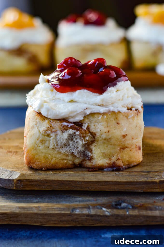 Perfect Homemade Cinnamon Rolls Recipe for Soft, Gooey Swirls 11 A front view of a cinnamon roll with cherry toppings on a wooden board with three cinnamon rolls in the background.
