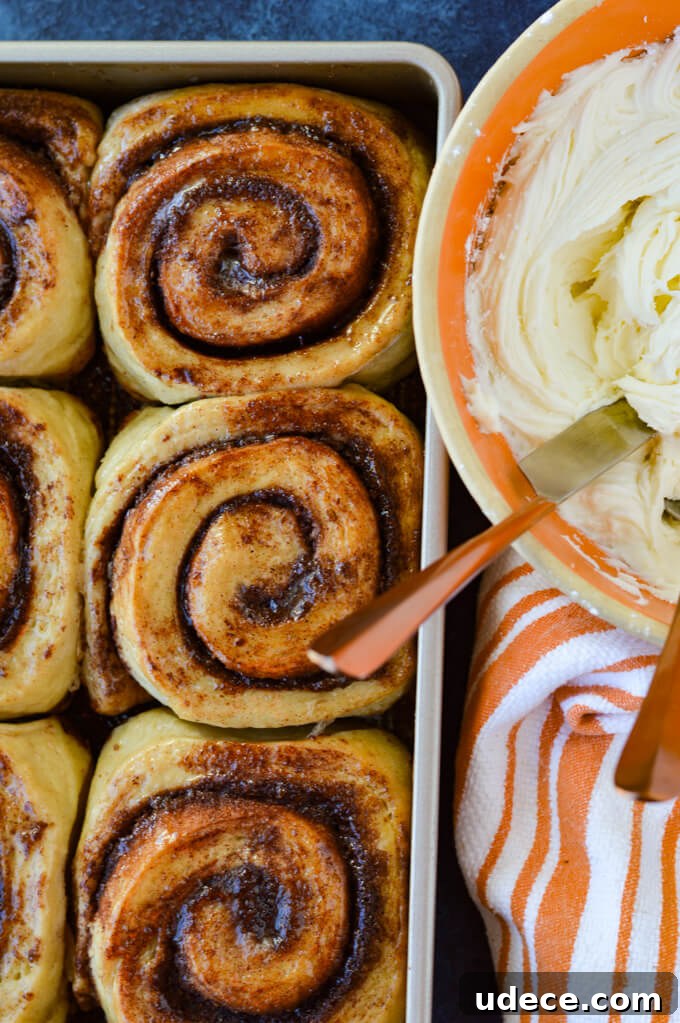 Perfect Homemade Cinnamon Rolls Recipe for Soft, Gooey Swirls 10 Baked cinnamon rolls in a pan with a bowl of icing beside it and an orange and white striped towel.