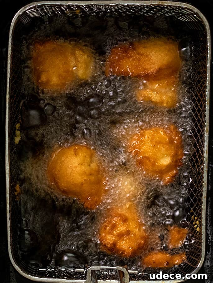 Five fritters frying in oil in frying basket overhead image