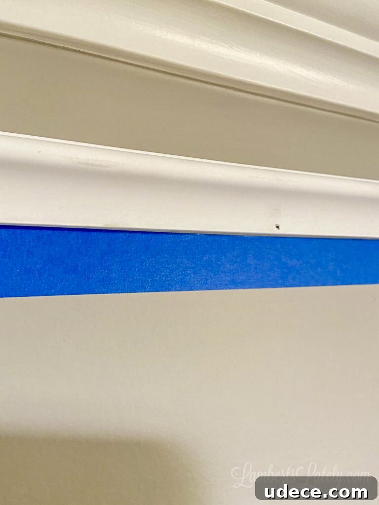 DIY Faux Crown Molding Guide: Simple Beginner-Friendly Hack 9 blue painters tape below molding piece on wall.