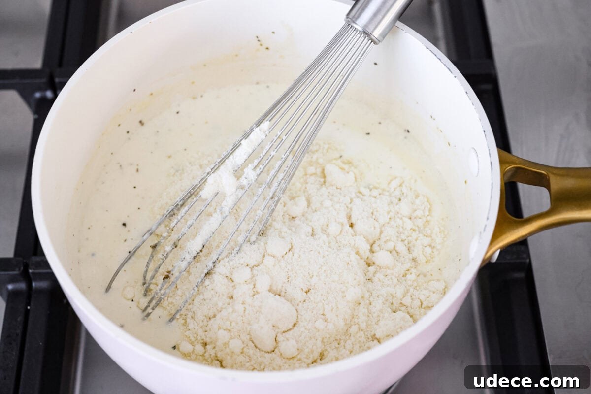 Creamy Baked Chicken Alfredo Pasta Casserole Recipe 4 Someone whisking the cheese into the sauce.