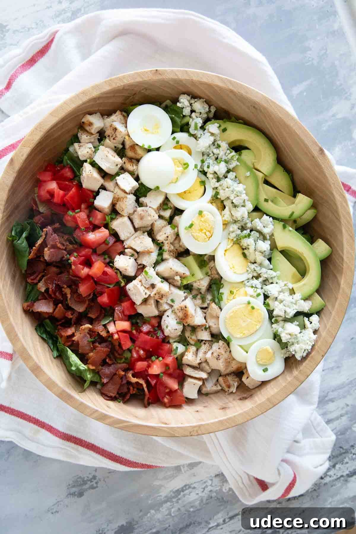 Classic Cobb Salad Recipe with Chicken, Bacon & Avocado 2 Cobb Salad with toppings arranged in lines on top in a large bowl.