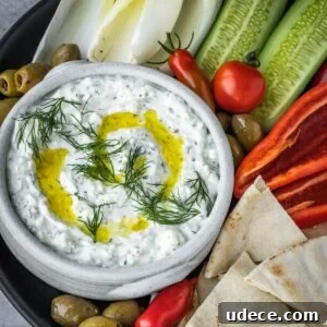 4 Mediterranean Meal Plans for Seasonal August Eating 8 Feta yogurt dip garnished with fresh dill and olive oil on a platter with olives, tomatoes, sliced cucumbers and pita bread triangles.