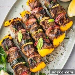4 Mediterranean Meal Plans for Seasonal August Eating 10 Middle Eastern Beef Shish Kebabs with yellow bell peppers, red onions, and zucchini on skewers, garnished with fresh mint and parsley. Served on a white platter with a lemon wedge and a small bowl of sauce.