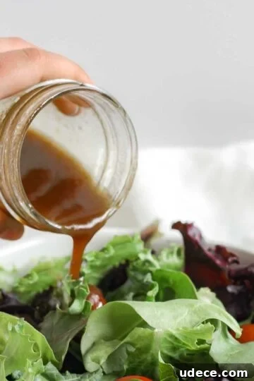 Balsamic vinaigrette being poured from a mason jar onto a bed of mixed greens.