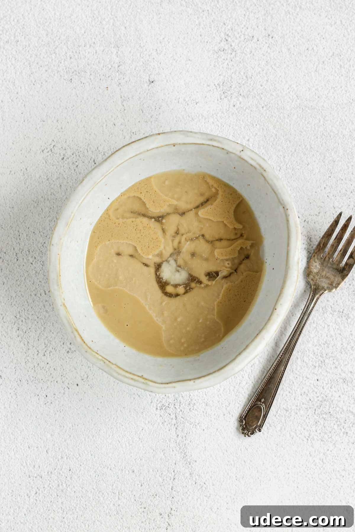 Maple Tahini Dressing Recipe for Salads and Bowls 4 Maple tahini salad dressing ingredients in a shallow bowl unmixed with a fork on the side of the bowl.
