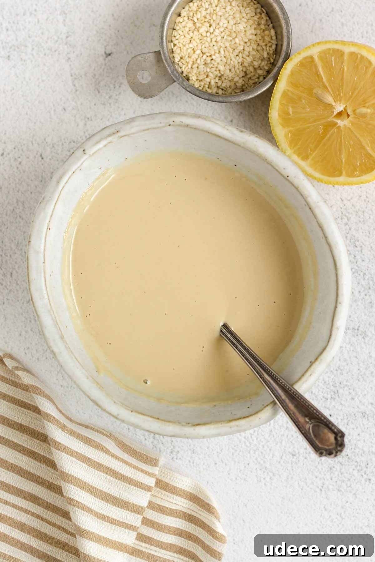 Maple Tahini Dressing Recipe for Salads and Bowls 7 Maple tahini dressing in a shallow bowl with a dish of sesame seeds and half a lemon on the side.