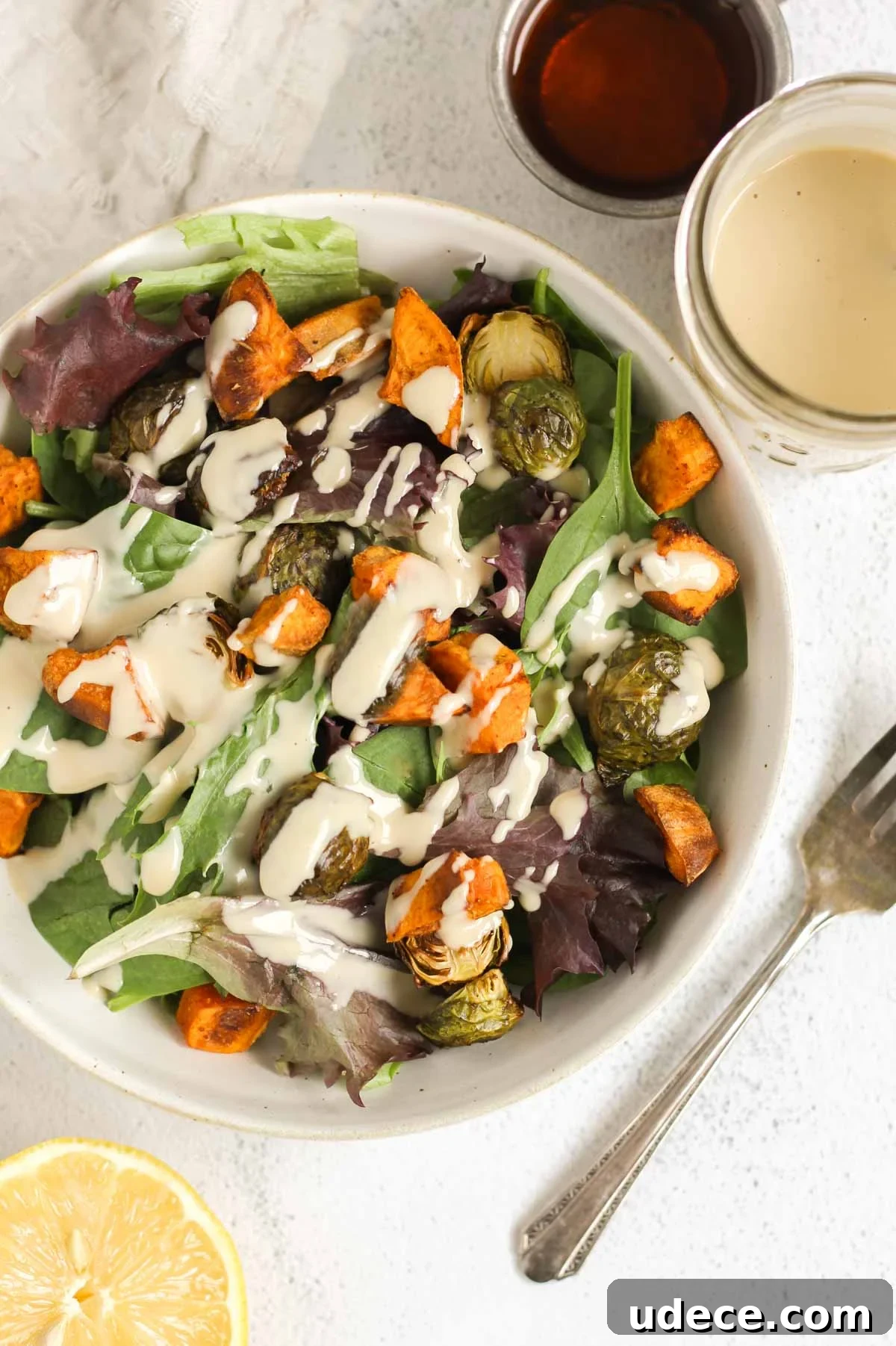 Maple Tahini Dressing Recipe for Salads and Bowls 8 A bowl of greens and roasted veggies with maple tahini dressing drizzled over the top with a fork on the side of the bowl.