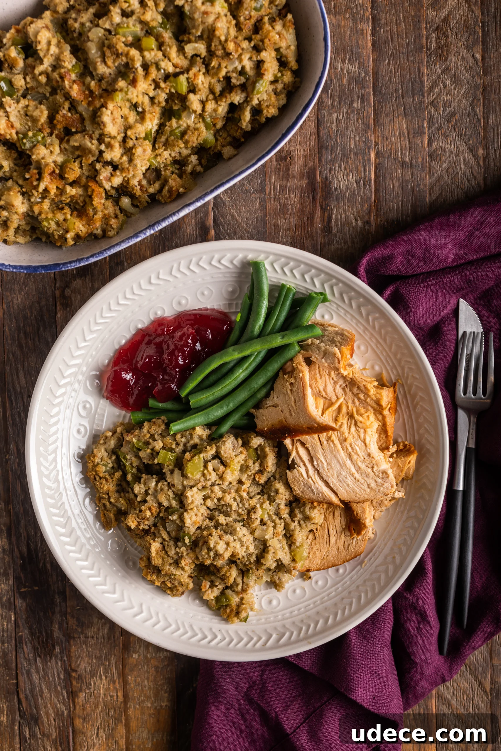Southern-Style Cornbread Dressing Recipe for Holidays 5 bowl of cornbread dressing next to a plate of cornbread dressing, turkey, green beans and cranberry sauce