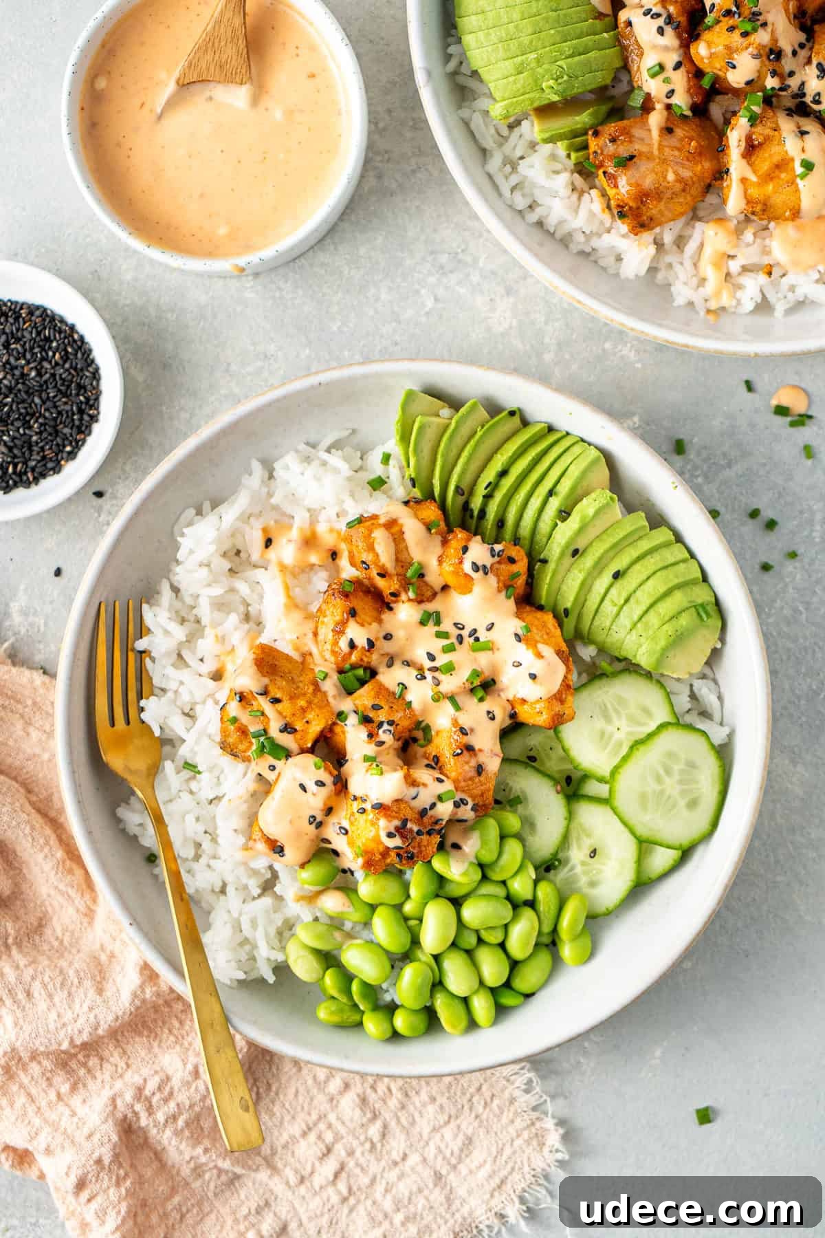 Bang bang salmon served in rice bowls with avocado, edamame and cucumber.