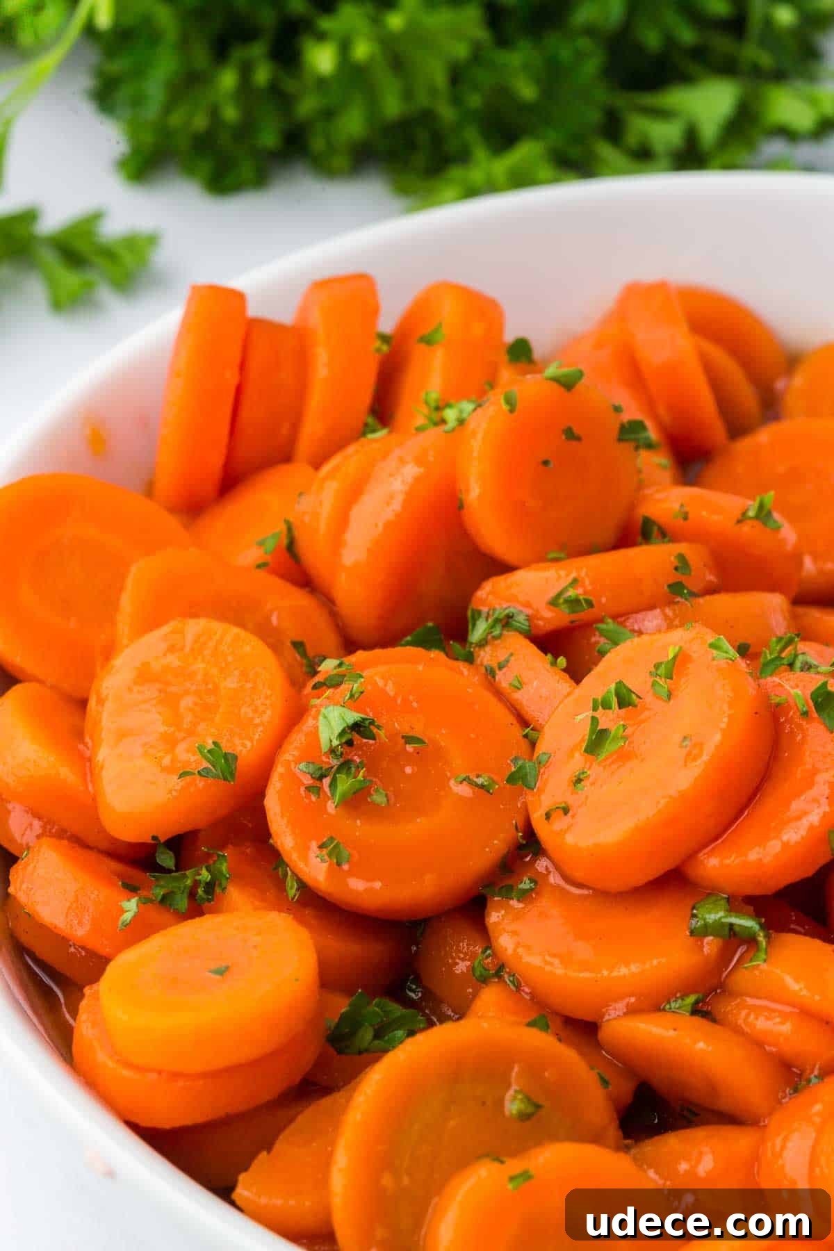 Close-up of a white bowl filled with glossy brown sugar and honey glazed canned carrots, garnished with fresh parsley.