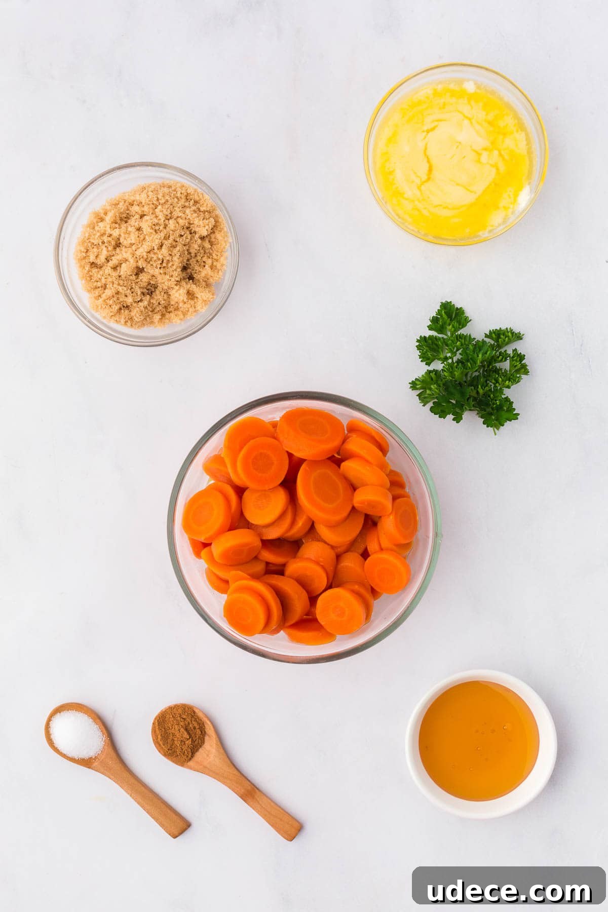 Flat lay of ingredients for brown sugar and honey glazed canned carrots including sliced canned carrots, brown sugar, melted butter, honey, cinnamon, salt, and fresh parsley.