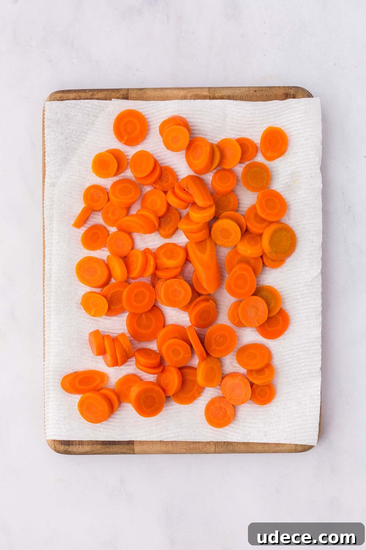 Sliced canned carrots drying on a paper towel-lined cutting board in preparation for glazing.