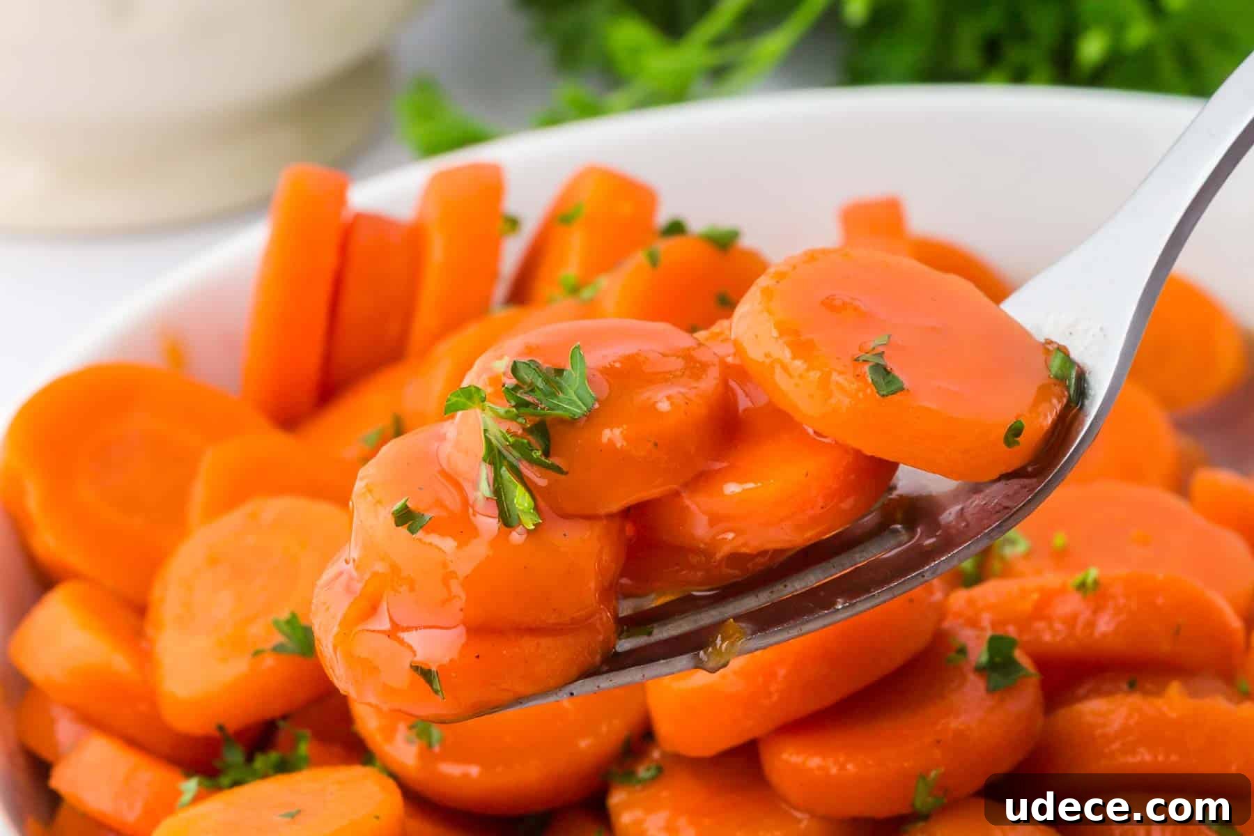 A fork lifting several slices of brown sugar and honey glazed canned carrots from a bowl, showing their shiny coating and parsley topping.