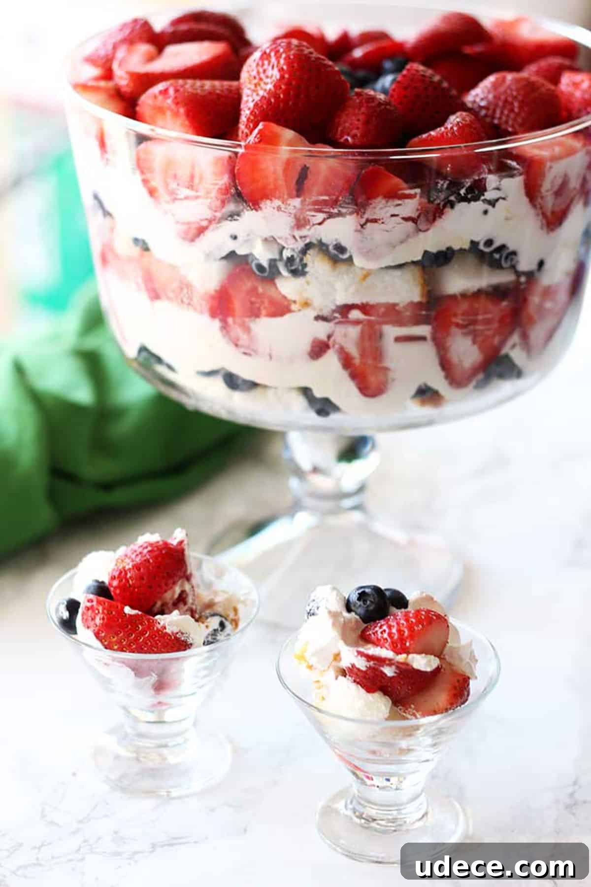 Trifle bowl containing cheesecake filling, angel food cake with strawberries and blueberries.
