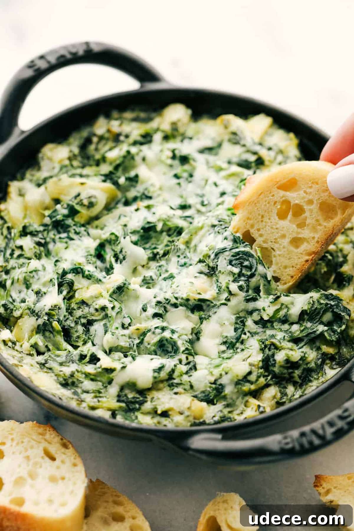Spinach and artichoke dip in a cast iron skillet, baguette being dipped into dip.