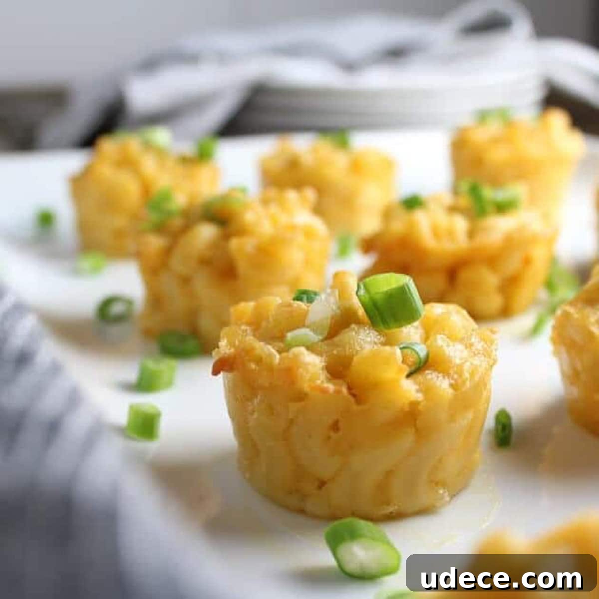 Mini macaroni and cheese cups on a table topped with chives.