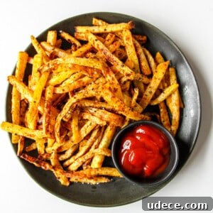 Rutabaga fries on a black plate with a small dish of ketchup.