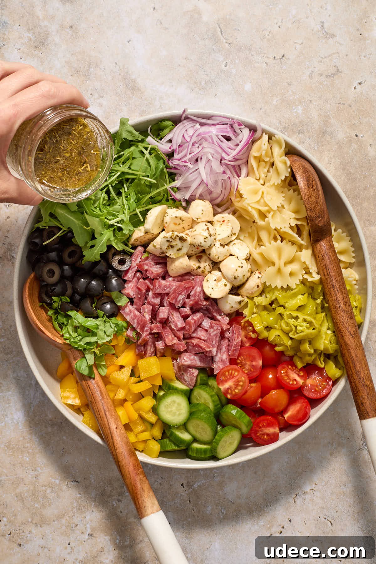 Salad ingredients sectioned in a bowl with vinaigrette being poured over the top.