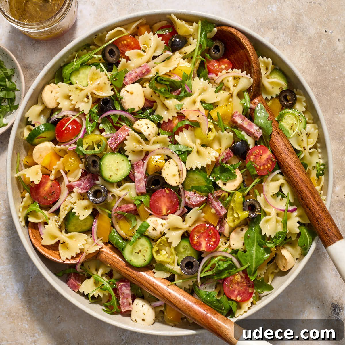 Italian bow tie pasta salad in a large bowl with wooden salad servers.