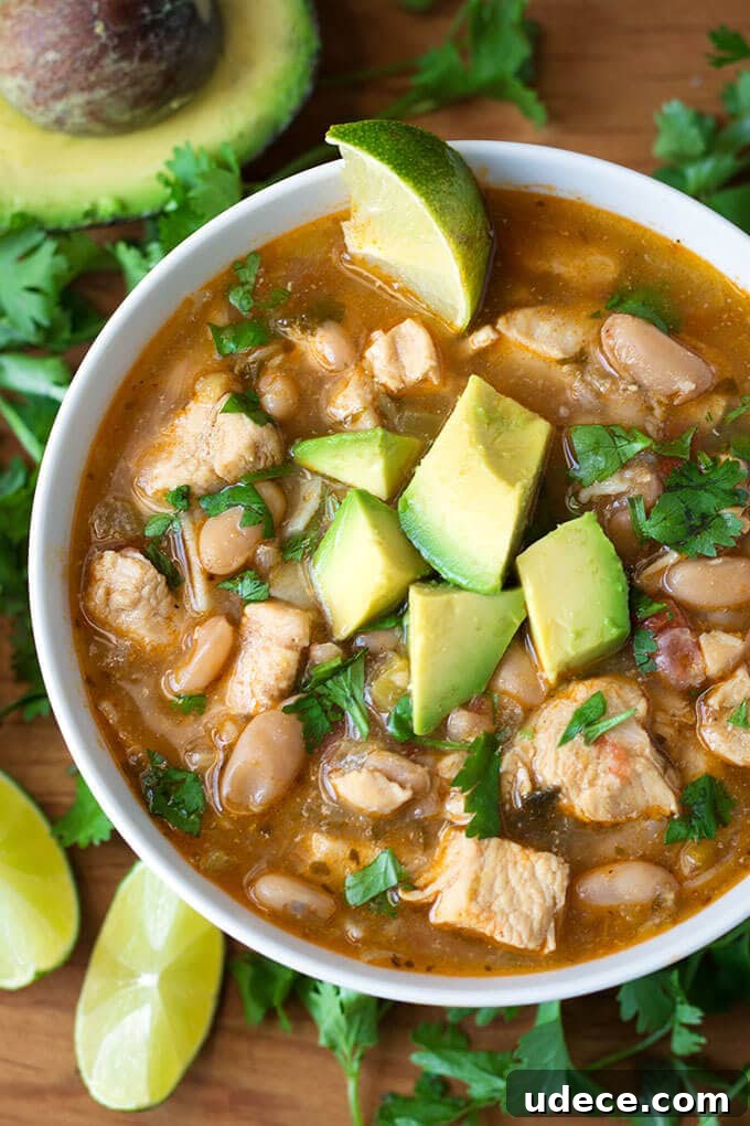 Creamy Instant Pot White Chicken Chili Recipe for Weeknights 2 Instant Pot White Chicken Chili in a white bowl topped with avocado surrounded by cilantro leaves and lime slices