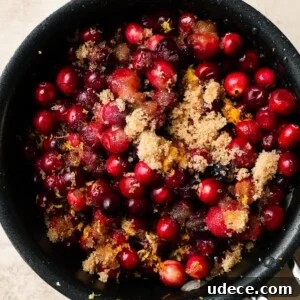Mandarin Orange Cranberry Sauce Recipe — Ready in 20 Minutes 10 Cranberries with brown sugar and orange zest in a black pot.