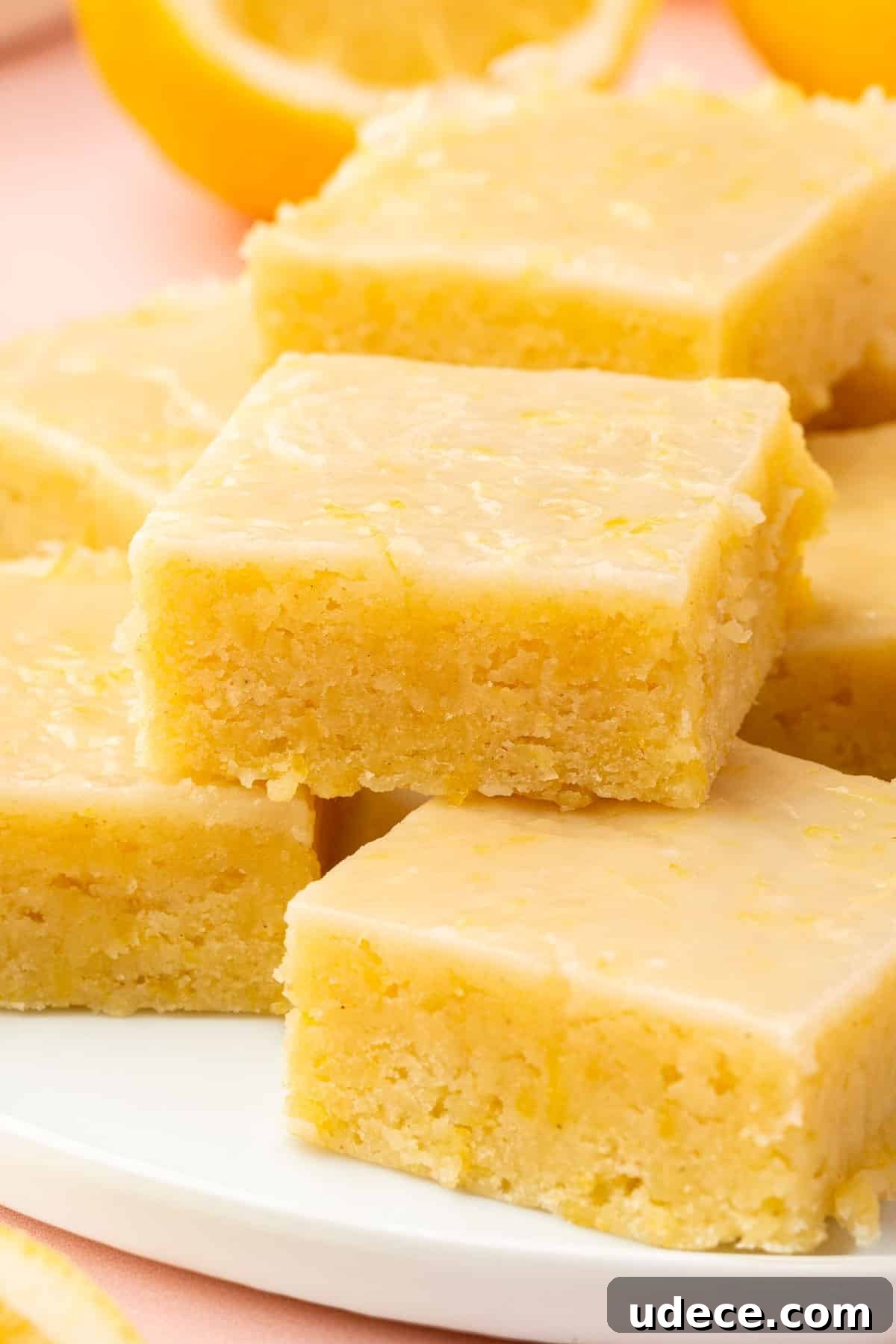Gluten-Free Lemon Brownies Recipe — Zesty Citrus Brownie Bars 2 A stack of gluten free lemon brownies with lemon glaze on a white dessert plate.