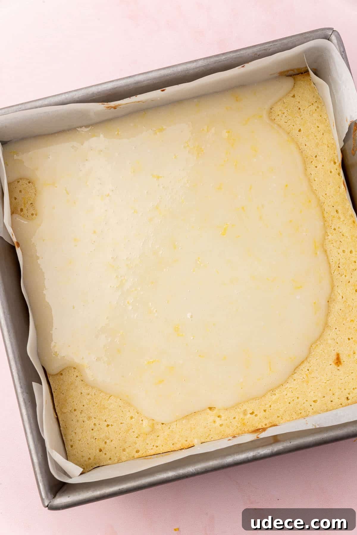 Gluten-Free Lemon Brownies Recipe — Zesty Citrus Brownie Bars 11 A square metal baking dish with lemon brownies that have been partially covered with lemon glaze.