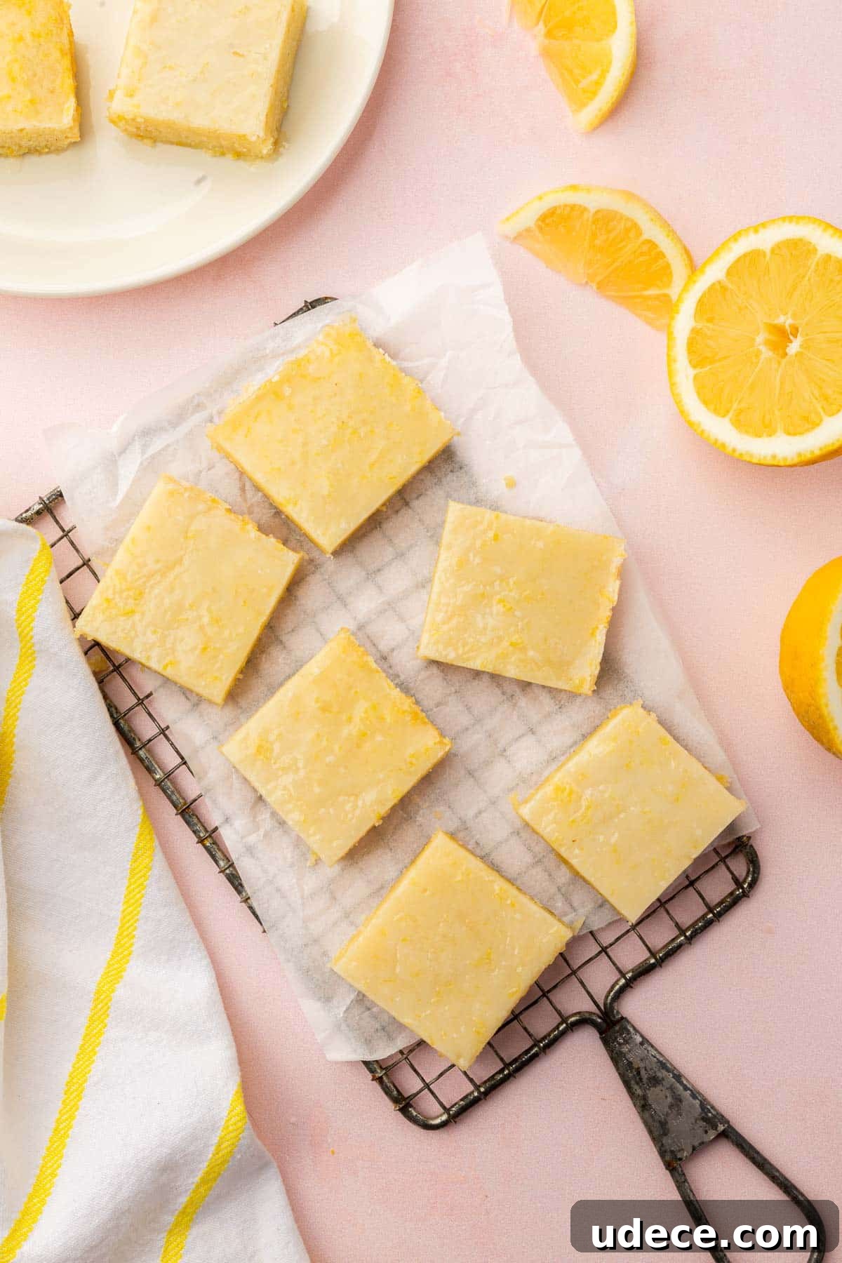 Gluten-Free Lemon Brownies Recipe — Zesty Citrus Brownie Bars 13 An overhead view of gf lemon brownies on a cooling rack with parchment paper with fresh lemon halves and slices on the side.