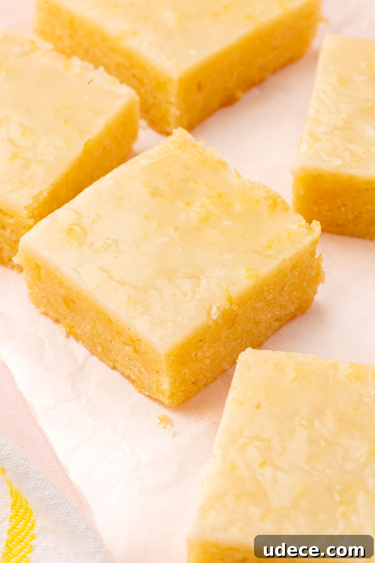 Gluten-Free Lemon Brownies Recipe — Zesty Citrus Brownie Bars 14 Square of gluten free lemon brownies with lemon glaze on a piece of parchment paper.